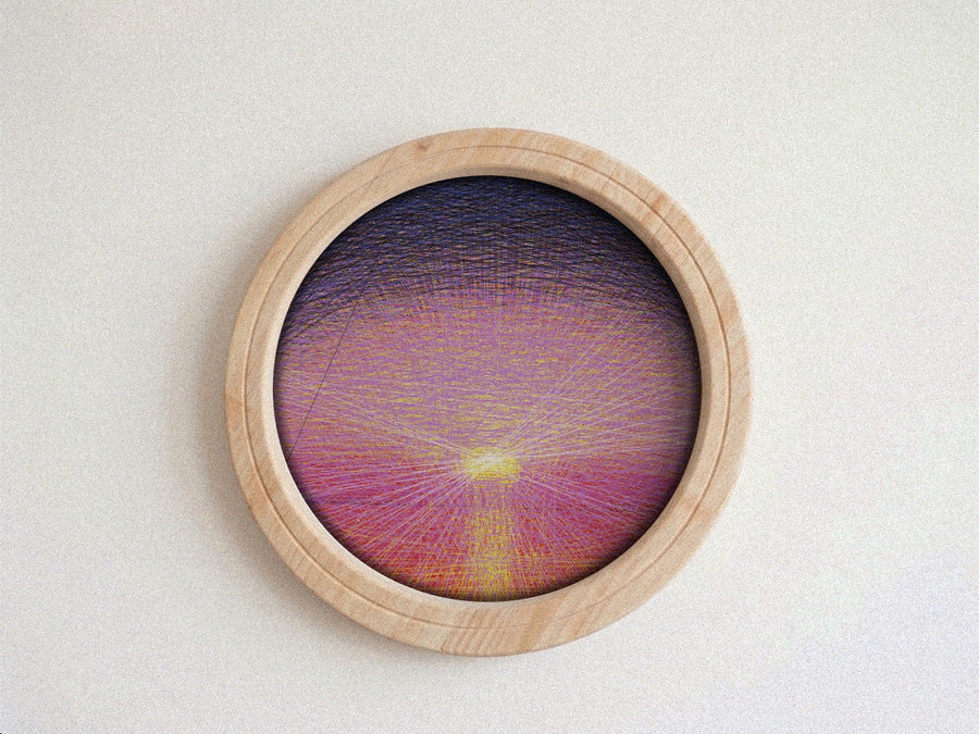 A circular wooden-framed string art piece featuring a colorful sunburst design with purple, pink, and yellow threads, displayed on a neutral textured background.