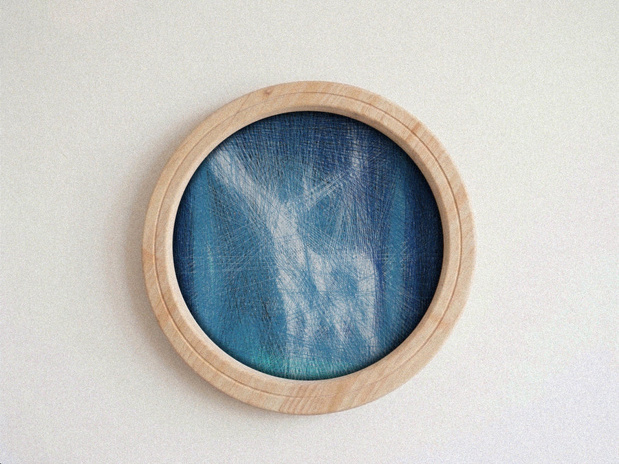 A round wooden-framed wall string art piece featuring a blue and teal textured mesh or fabric design, mounted on a plain off-white wall.