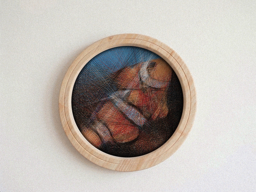 A circular wooden-framed string art featuring a colorful abstract or painted scene with a blue background and warm orange, red, and brown tones, mounted against a plain light wall.