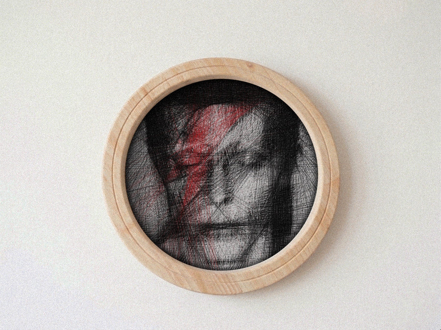 A circular wooden-framed portrait string art featuring a black-and-white sketch of David Bowie with a bold red lightning bolt on his face, mounted against a plain light background.