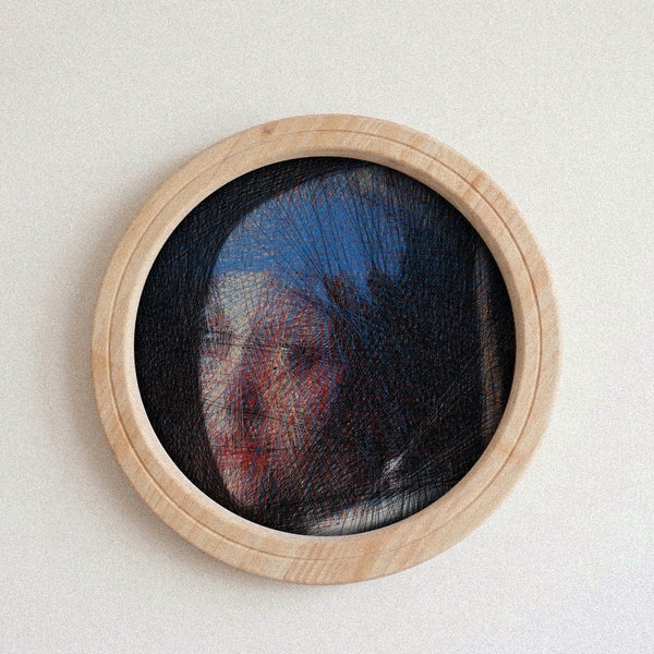 A circular wooden-framed needlework string art piece featuring a portrait of a woman in profile, set against a plain off-white wall.