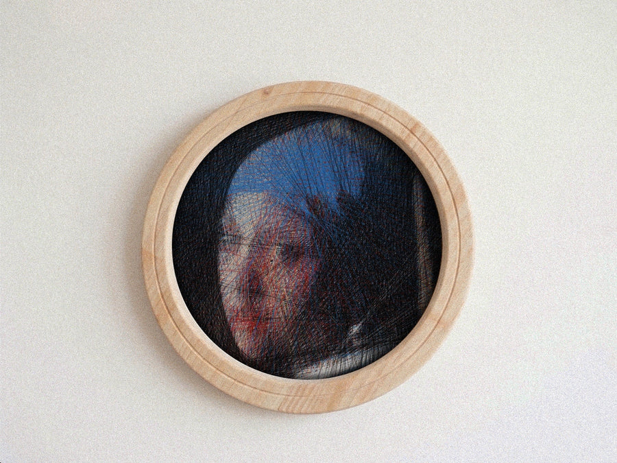 A circular wooden-framed needlework string art piece featuring a portrait of a woman in profile, set against a plain off-white wall.
