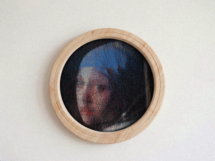 A circular wooden-framed needlework string art piece featuring a portrait of a woman in profile, set against a plain off-white wall.