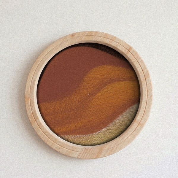 A round wooden-framed string art piece featuring an abstract textured design in warm earthy tones of brown, orange, and beige, mounted on a plain off-white wall.