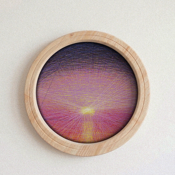 A circular wooden-framed string art piece featuring a colorful sunburst design with purple, pink, and yellow threads, displayed on a neutral textured background.