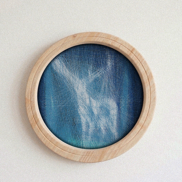 A round wooden-framed wall string art piece featuring a blue and teal textured mesh or fabric design, mounted on a plain off-white wall.