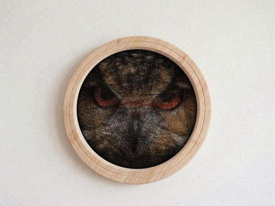 A circular wooden wall string art piece featuring a dark, textured cat face with prominent red eyes, mounted on a plain off-white wall.