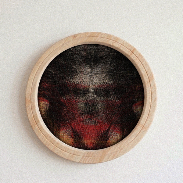 A circular framed string art work featuring a dark, textured face with red and orange details, set in a light natural wood frame against a plain off-white wall.