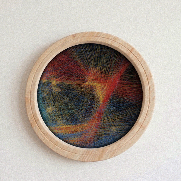 A circular framed abstract string art piece with colorful lines on a dark background, mounted on a light textured wall.