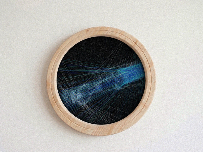 A circular framed string art piece featuring a blue and white abstract design on a black background, housed in a light natural wood frame against a neutral off-white wall.