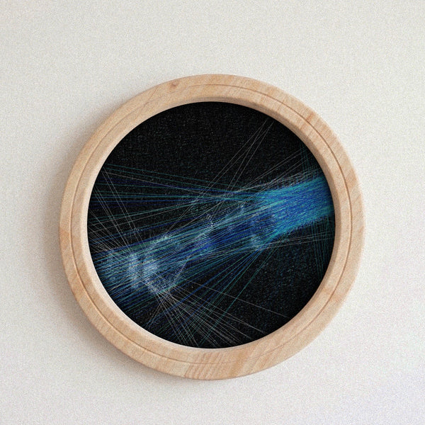 A circular framed string art piece featuring a blue and white abstract design on a black background, housed in a light natural wood frame against a neutral off-white wall.