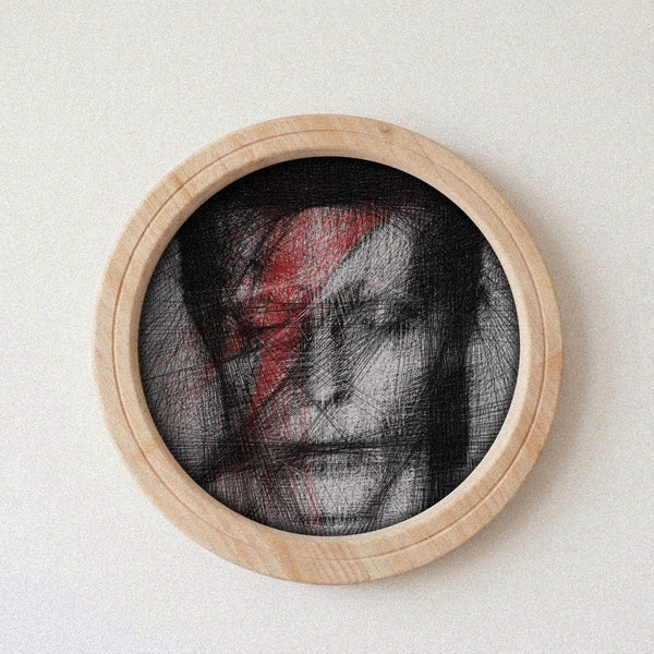 A circular wooden-framed portrait string art featuring a black-and-white sketch of David Bowie with a bold red lightning bolt on his face, mounted against a plain light background.