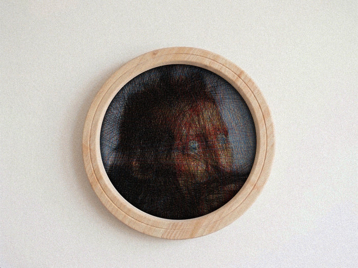 A circular wall string piece featuring a portrait of a woman's face created with thread over a dark mesh background, framed in a light natural wood border, mounted on a plain off-white wall.