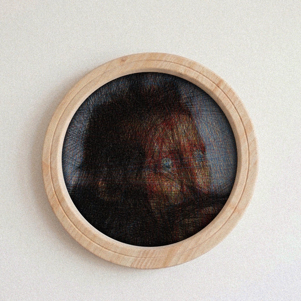 A circular wall string piece featuring a portrait of a woman's face created with thread over a dark mesh background, framed in a light natural wood border, mounted on a plain off-white wall.