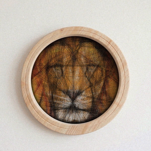 A circular wooden framed string art piece featuring a lion face created with dense black string over a warm brown and orange background, mounted on a light textured wall.