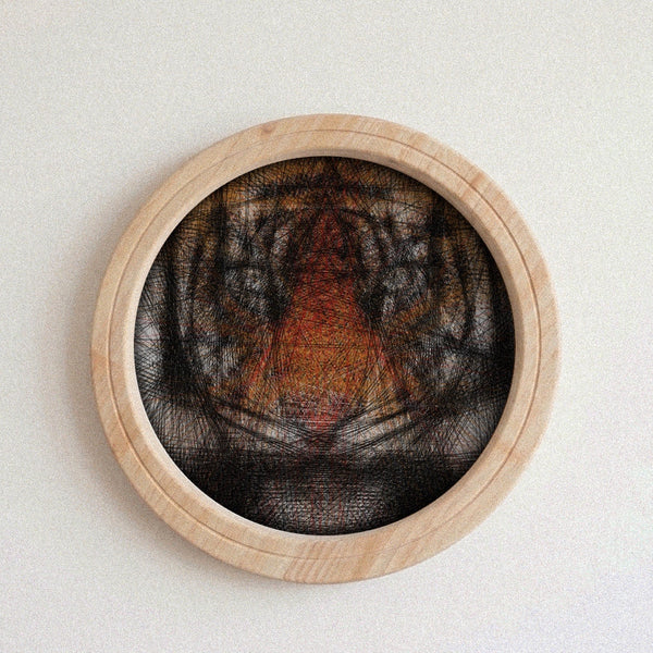 A circular wooden wall string art piece featuring a black, gray, and orange tiger face design, mounted on a plain off-white wall.