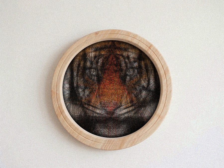 A circular wooden wall string art piece featuring a black, gray, and orange tiger face design, mounted on a plain off-white wall.